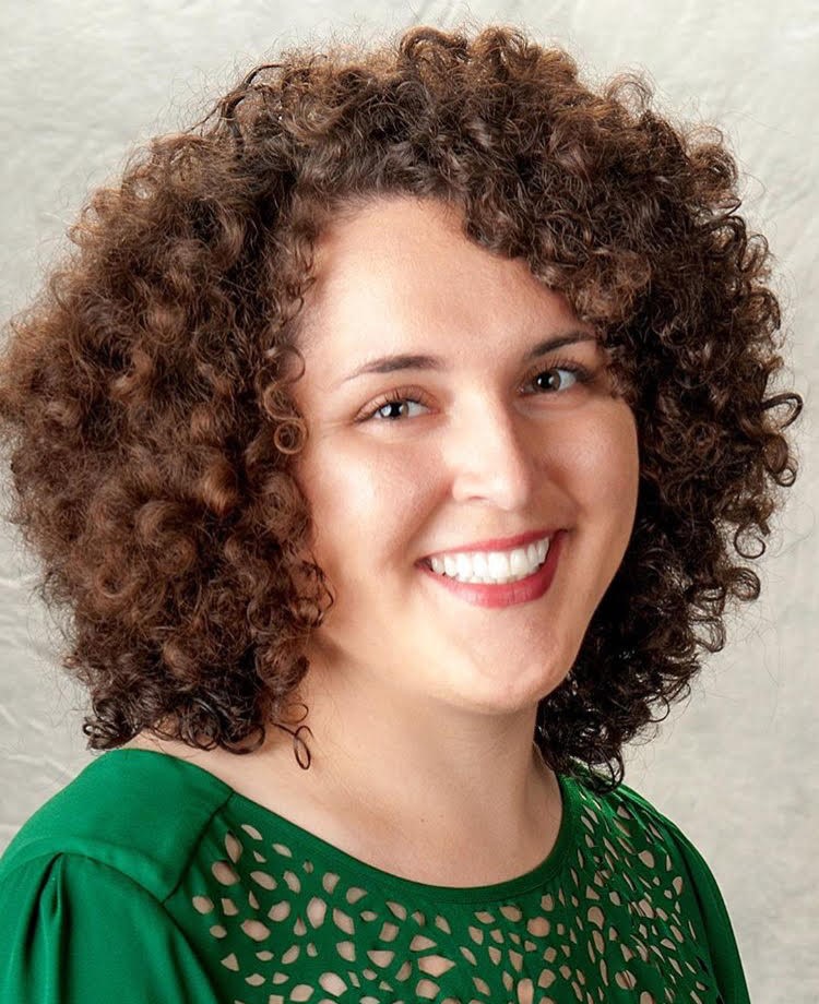 images shows head and shoulders of a smiling light skinned woman with dark curly hair wearing a green shirt