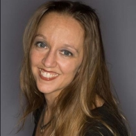 image shows face and shoulders of a smiling light skinned woman with light brown should length hair wearing a black shirt