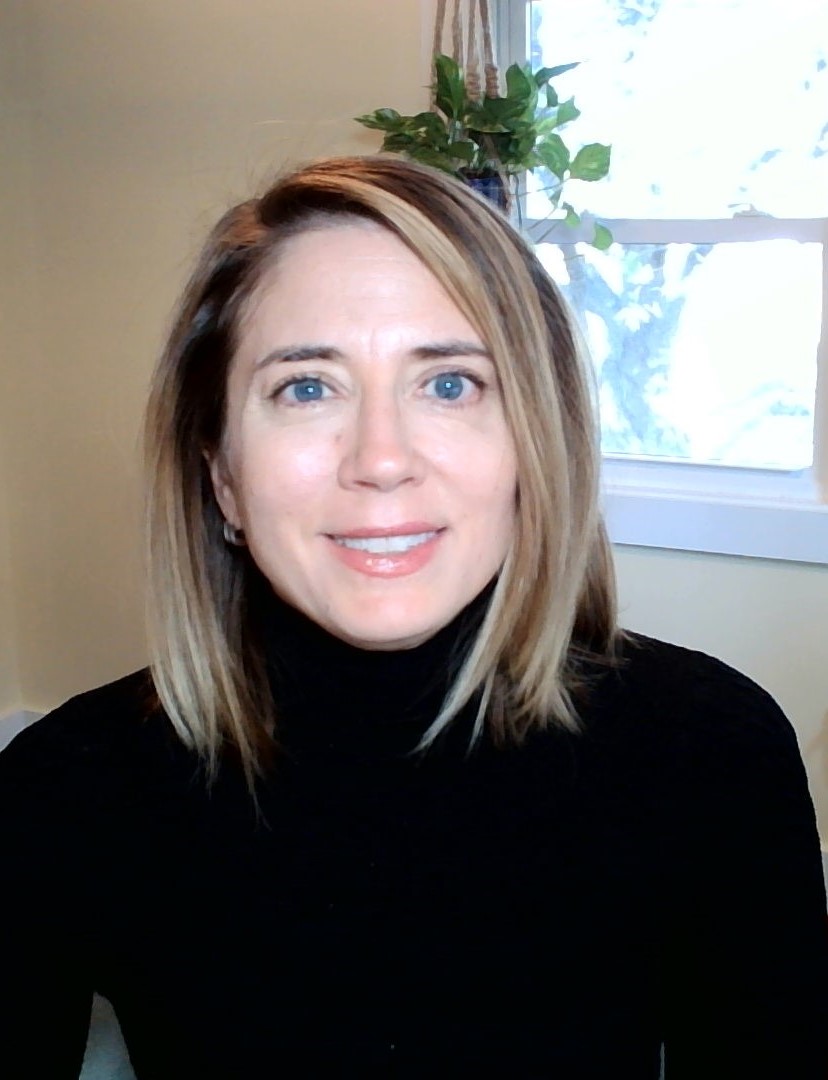 image shows the head and shoulders of a smiling light-skinned woman with shoulder length light brown hair wearing a black turtle neck.