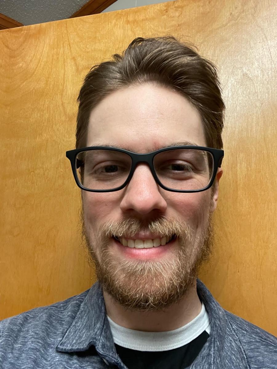 IImage shows the head and upper shoulders of a light-skinned man with medium-brown, short hair and a beard wearing glasses and a blue collared shirt